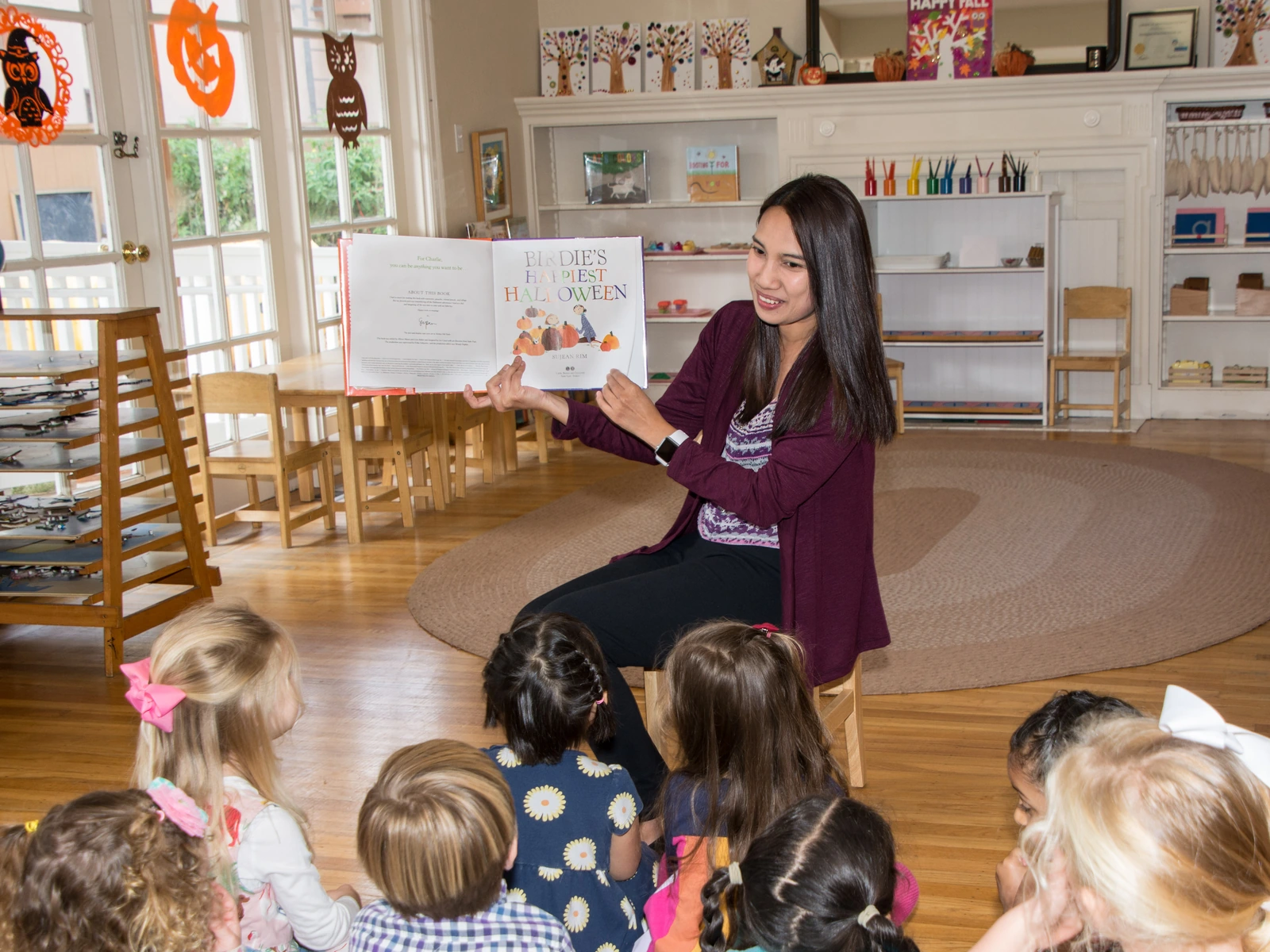 A teacher reading aloud to children gathered on the classroom rug